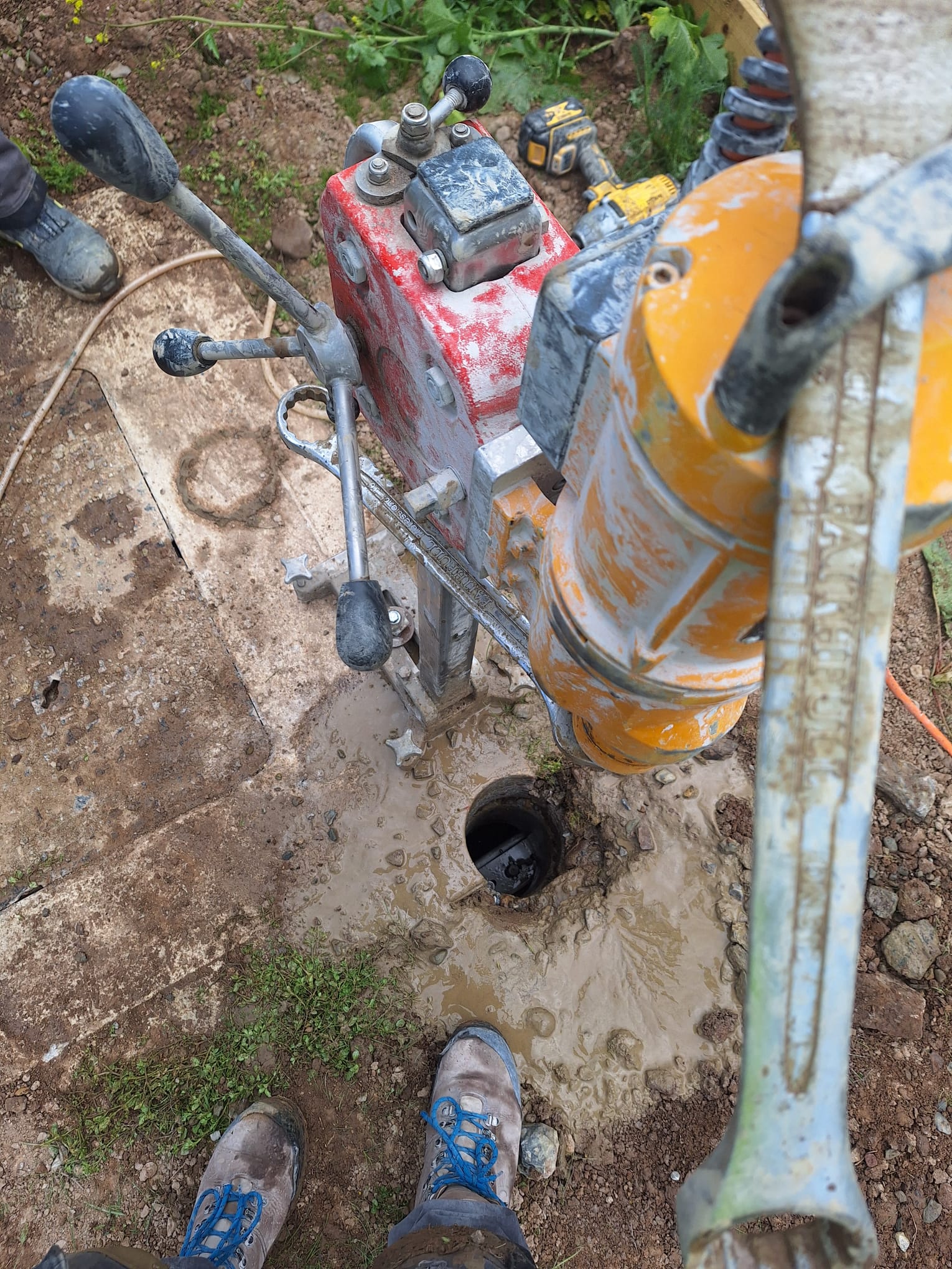 Rig-mounted diamond core drill boring through outdoor concrete slab for manhole access — water suppression active, operator in hi-vis