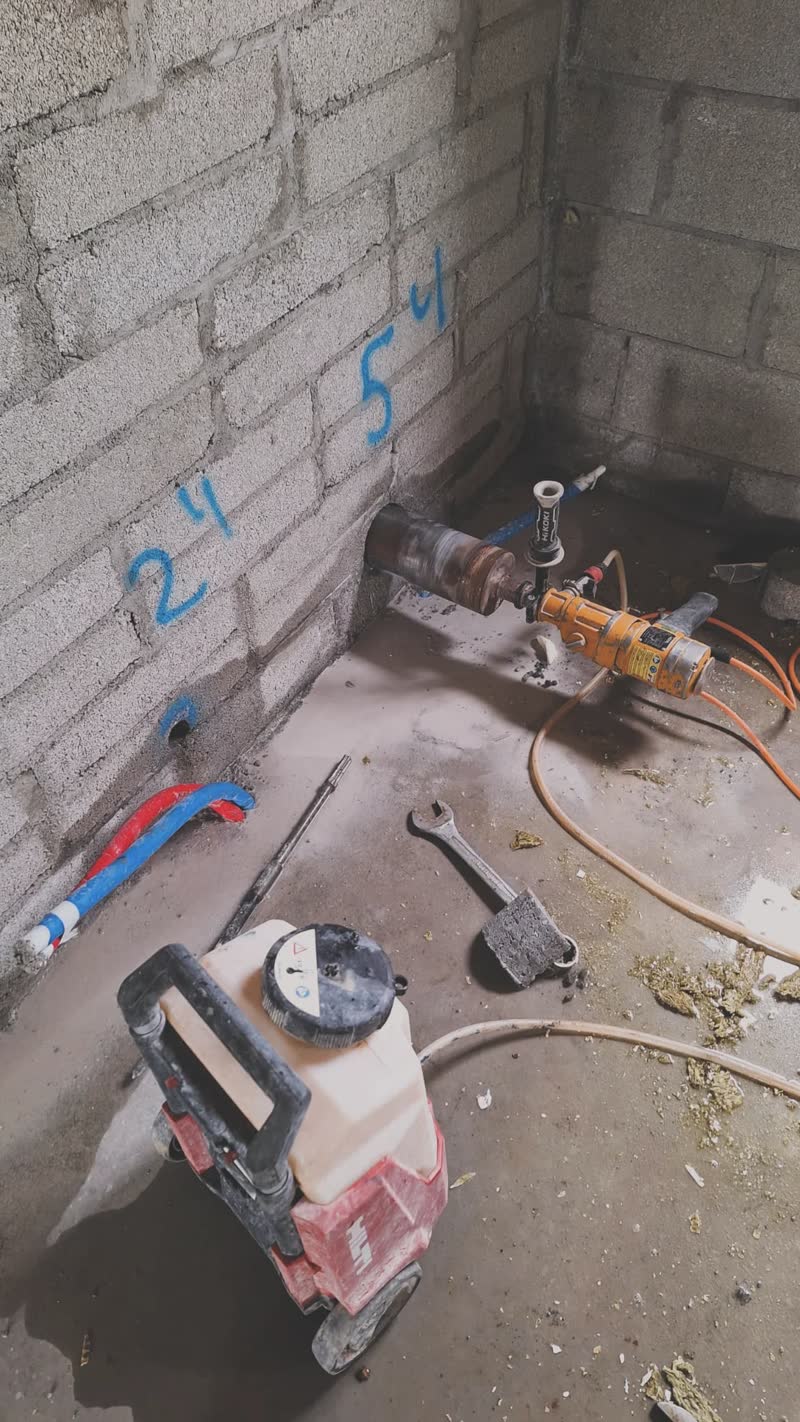 Hand-held core drill set up on marked pipe penetration points through blockwork, sized in inches